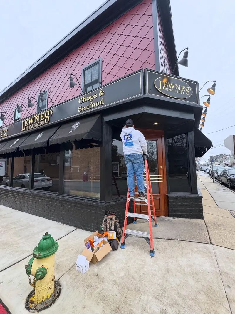 Energetic Electric electrician on a ladder working on exterior lighting at a restaurant